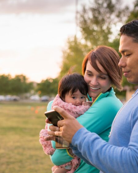 Para z dzieckiem, korzystająca z telefonu komórkowego w parku