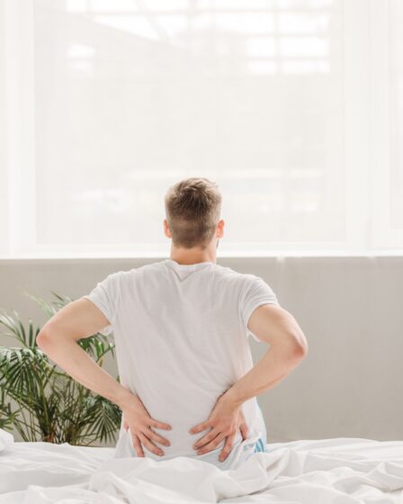 widok z tyłu mężczyzny dotykającego pleców siedzącego na łóżku i cierpiącego na ból