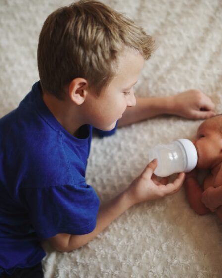 młody chłopiec karmi noworodka butelką mleka